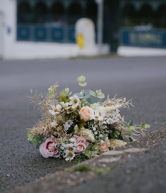 A delicate floral bouquet featuring soft pink roses, small white daisy-like flowers, and light green eucalyptus and foliage, arranged in a natural, loose style. The bouquet is placed on the pavement n